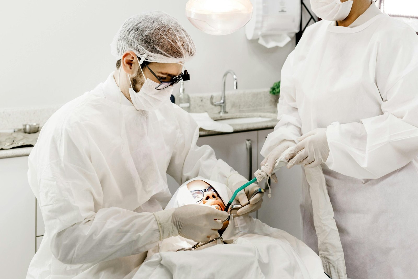 From above of unrecognizable male stomatologist and female assistant in uniforms treating patient teeth in clinic